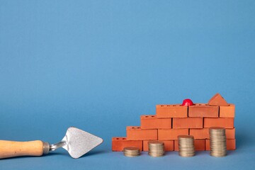 Stacks of coins in the form of steps against a background of red brickwork and a masonry trowel. Construction investment concept