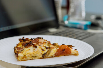 Piece of freshly baked pizza lies on a plate near the computer