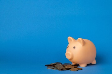 Pink piggy bank and coins on a blue background. Money saving and deposit concept