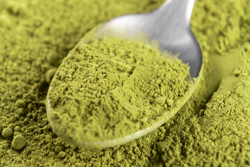 Metallic teaspoon with powdered matcha green tea in heap of powder