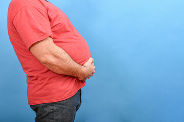 Fat and fat man with a big belly in jeans and a red T-shirt on a blue background.