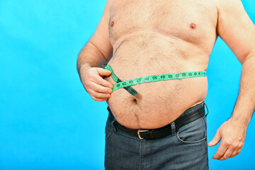 A man in jeans measures a large fat waist with a green centimeter.