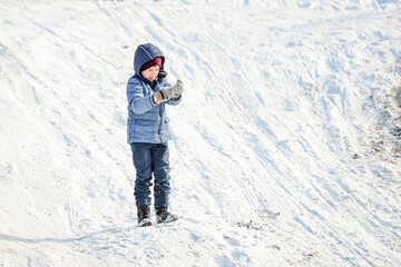 Fototapeta na wymiar The boy straightens his mittens in the snow after playing snowballs.