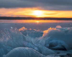 the sun shines through the ice at sunset, on the shore of a forest lake covered with snow in cold winters.