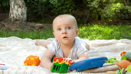 Portrait of smiling baby boy playing toys on picnic at park. Concept of child early development, education and relaxing outdoors.