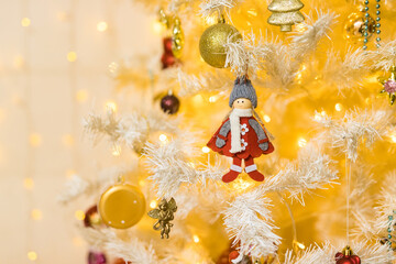 Close up of red doll toy and garlands on white yellow Christmas tree