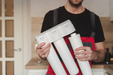 Plumber in the kitchen holding household three stage flask water purification system