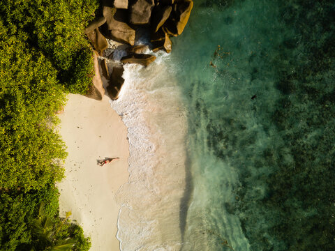 Colorful ocean shore, red bikini dressed pretty woman lays on sand, next to the waves.