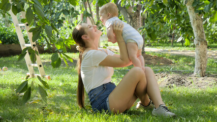 Happy family in garden. Mother playing with little baby boy on grass at orchard