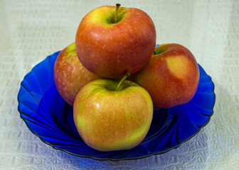 Four apples are on a blue plate. Red and yellow apples. Fruit. Healthy lifestyle. Proper nutrition. Fruits containing vitamins.
