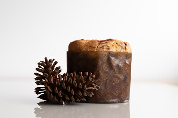 Christmas panettone with pine cones on the side, on a white glass table, reflection on a table, horizontal photo with space for text