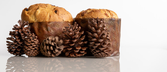 Christmas panettones with pine cones on the side, on a white glass table, reflection on the table, horizontal close-up photo with space for text.