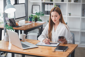 Businesswoman or accountant using the phone to check business information. Accounting Documents and Laptop at Small Office Business Ideas