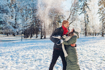 Happy young couple playing with snow in winter park. Man and woman having fun outdoors.