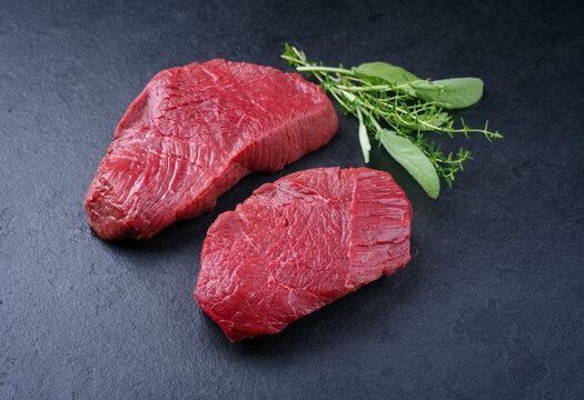 Rohe dry aged Bison Rumpsteaks vom Rind als St&uuml;ck und Scheiben angeboten als close-up auf schwarzem Hintergrund mit Textfreiraum
