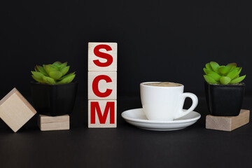 SCM. Three wooden blocks on dark background. red notepad. a cup of coffee