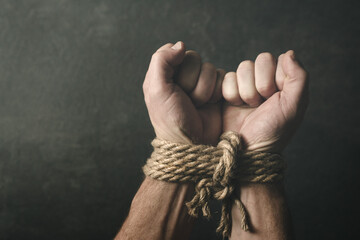 Male hands tied with a rough rope at the wrists close-up on a dark background, soft focus. Conceptual image of violence, slavery, dependence, lawlessness, lack of freedom - obrazy, fototapety, plakaty