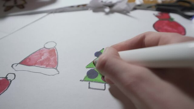 Child colouring Christmas tree with pencil and drawing toy balls POV view from above