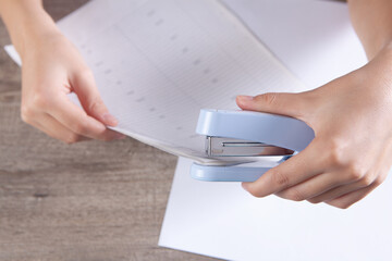 woman connects papers with a stapler - obrazy, fototapety, plakaty