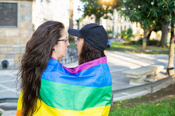 Couple of lesbian girls with LGBT pride flag laughing in park