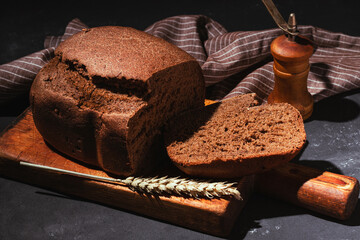 Freshly baked brown rye bread sliced ​​on wooden cutting board on black background