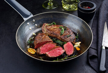 Traditional fried dry aged bison beef rump steaks with herbs and garlic served as close-up in a...