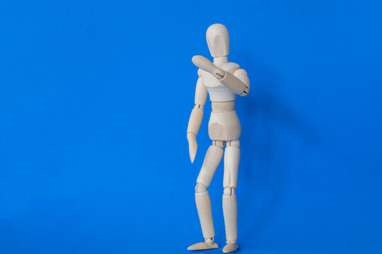 Isolated wooden manikin with raised arm on blue background.