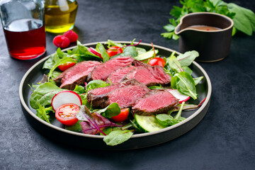 Modern style traditional fried dry aged bison beef rump steak slices with vegetable, lettuce and mustard dressing served as close-up on a Nordic design plate