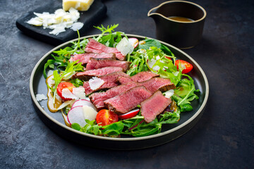 Modern style traditional fried dry aged bison beef rump steak slices with vegetable, lettuce and mustard dressing served as close-up on a Nordic design plate