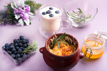 earthenware pot with baked potatoes and baked cheese. A cup of milk with blueberries and a jar of honey