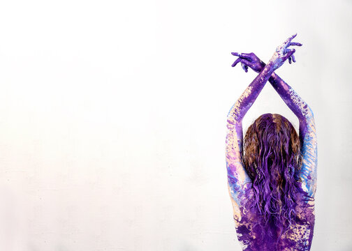 Back view and crossed raised arms of young artistically abstract painted woman, ballerina with white, blue and purple, violet paint, Creative body art painting