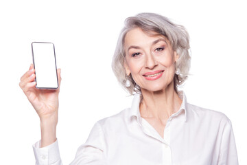 Close up portrait of an attractive happy modern mature woman looks at the camera with a smile showing a smartphone in her raised hand isolated on white background