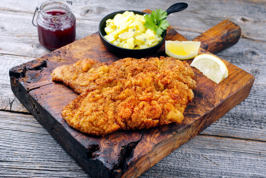 Traditionelles frittiertes Schnitzel mit Kartoffelsalat und Preiselbeeren serviert als close-up auf einem alten rustikalen Holz Board in einer Bergh&uuml;tte