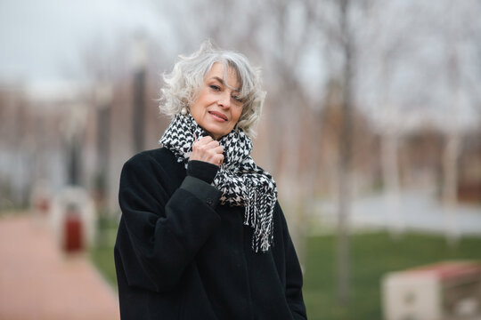 Portrait of a beautiful mature woman walking in autumn park in a coat and warm trendy scarf