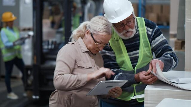 Female inspector checks quality manufactured goods, asking questions elderly worker man. Inspection concept. Concept of checking goods in a paper production warehouse