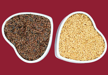 Brown and golden flax seeds in ceramic bowls of heart shape, red background, isolated 