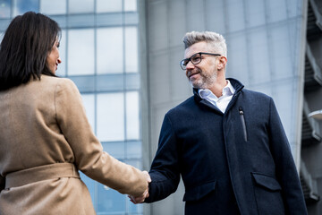 Business man shaking hands with partner in front of office buildings in the city - greeting, dealing, merger and acquisition concepts