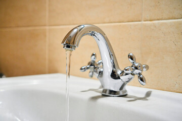 Common mixer tap. Water flowing out of bathroom stainless steel pillar tap into sink. Wasting water...