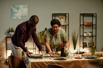 Waist up portrait of two African-American people serving table for family dinner party at home, copy space