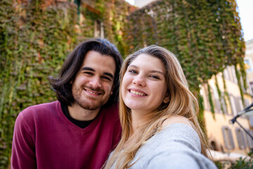 Obraz premium Beautiful couple traveling to Rome. Young couple takes a selfie in a street in the historic center. In the background a building covered with ivy.