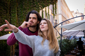 Naklejka premium Beautiful couple traveling to Rome. A blonde woman points the way to her boyfriend. Young people are looking in the same direction.