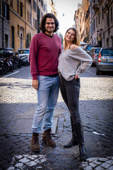 Fototapeta na wymiar Beautiful couple traveling to Rome. A young couple poses for a photo in the streets of the historic center of the city. In the background buildings and cars.