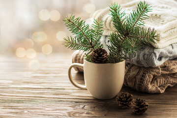 Cozy winter. Fir branches with cones in a mug on a background of knitted sweaters. Knitwear, wooden...