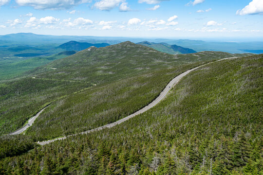 Wide angle view overlooking dense green forest with road cutting across it and mountains in the horizon near Adirondack National Park