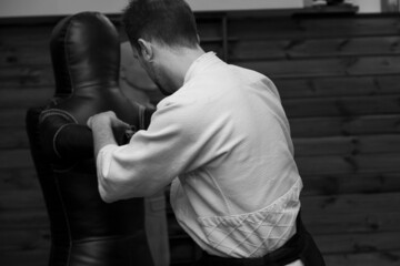 a man in a kimono and a hakama practicing blows on a sports dummy