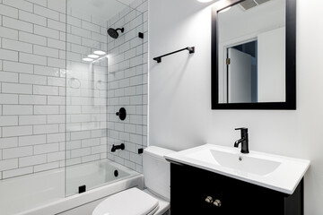 A small modern bathroom with a dark vanity, mirror frame, and hardware. White subway tiles line the...