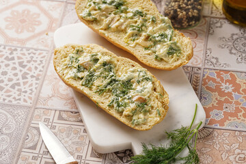 Two halves of garlic and butter bread - baguette on a marble board, sea salt, pepper, dill and...