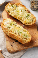 Two halves of garlic and butter bread - baguette on a wooden board, sea salt, pepper, dill and garlic cloves on a grey concrete background, top view