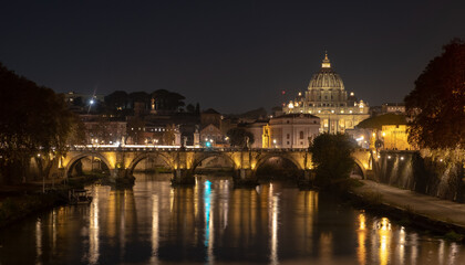 Fototapeta premium View of the St. Peter's basilica dome with the Vittorio Emanuele II bridge at the foreground, Vatican City, Rome. Light reflection in the water of the Tiber river in the late evening.