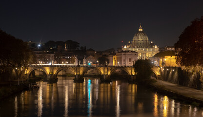 View of the St. Peter's basilica dome with the Vittorio Emanuele II bridge at the foreground, Vatican City, Rome. Light reflection in the water of the Tiber river in the late evening.